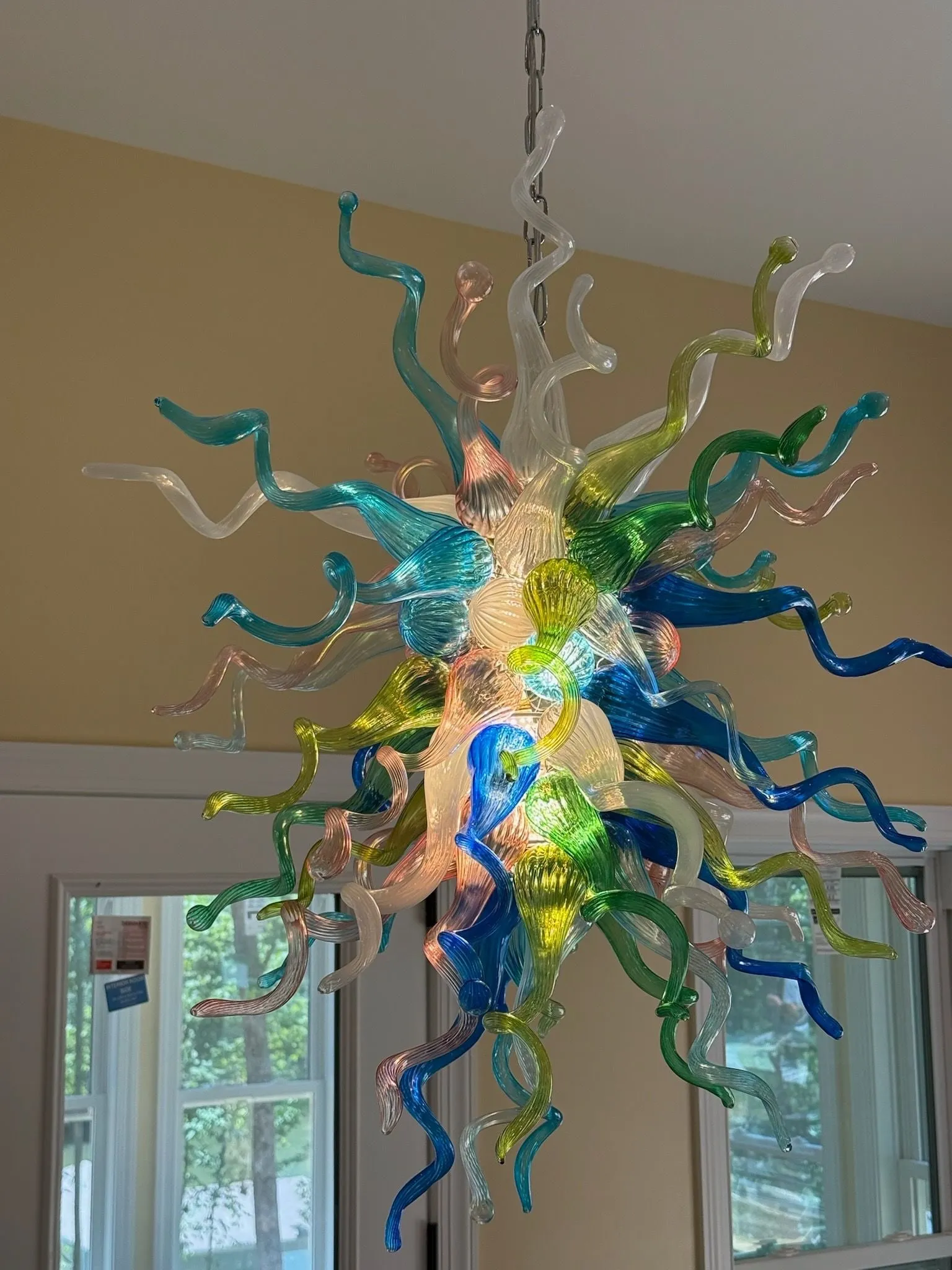A blown-glass chandelier of twisting blue, green, amber and clear glass arms hanging in a bright room