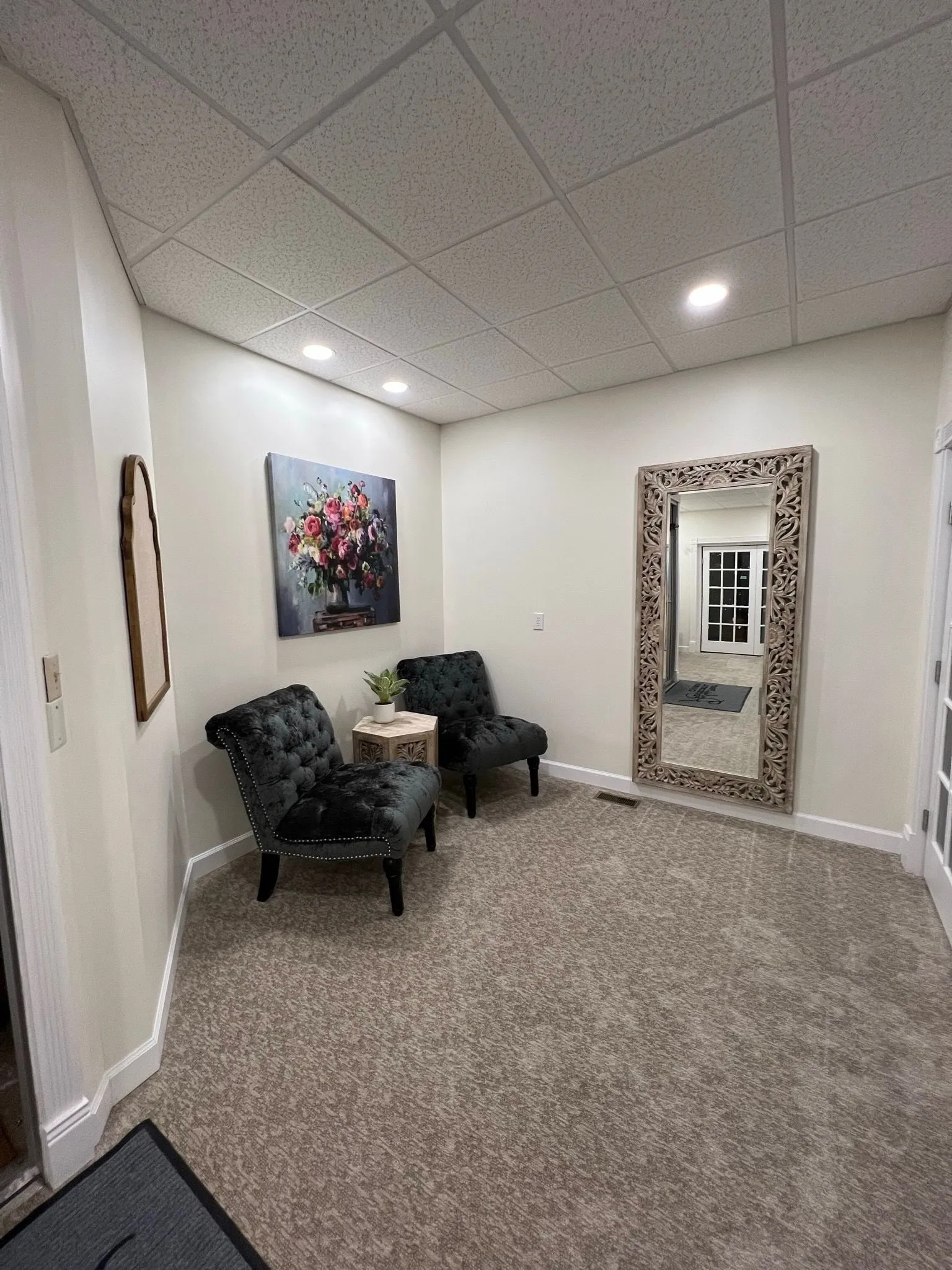 A small carpeted room with two chairs and a tall mirror, lit by recessed ceiling lights