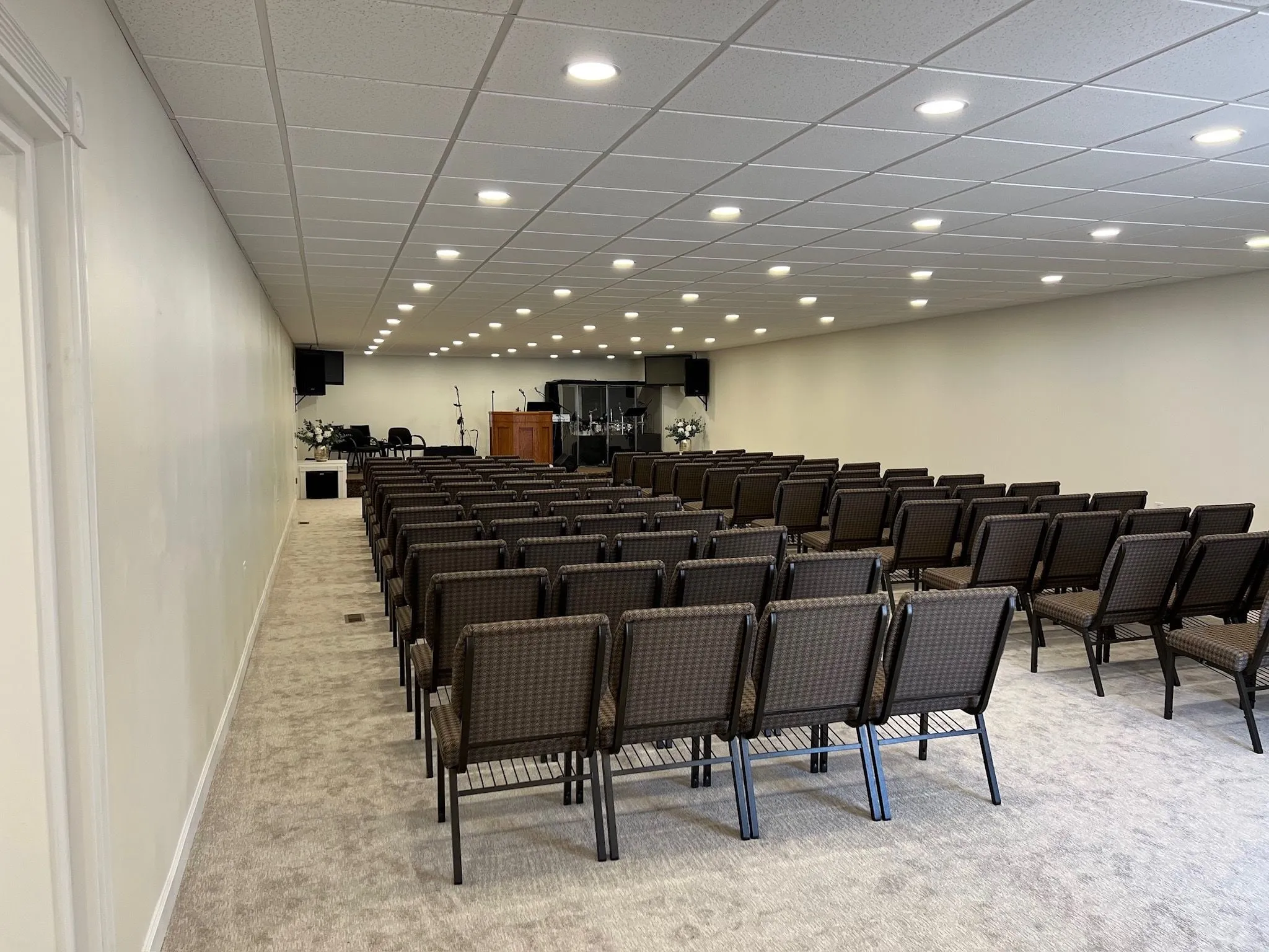 An auditorium with rows of chairs facing a pulpit, lit by rows of recessed ceiling lights
