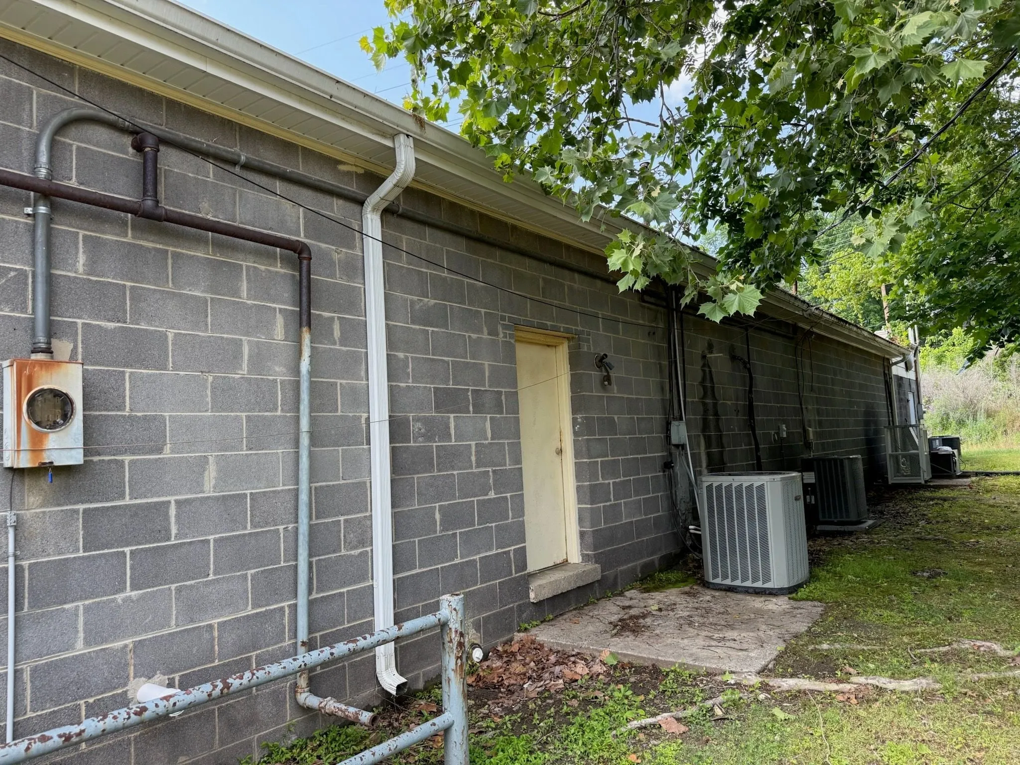 The back wall of a block building with an old electrical meter at one end and conduit running along the wall
