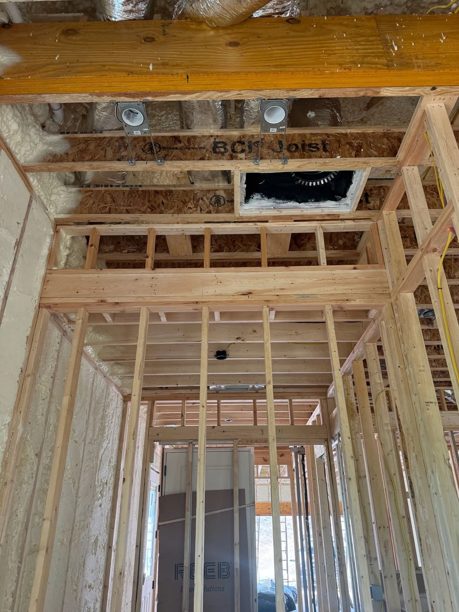 Looking up into the open framing of a new house, with two recessed light housings already fixed between the ceiling joists