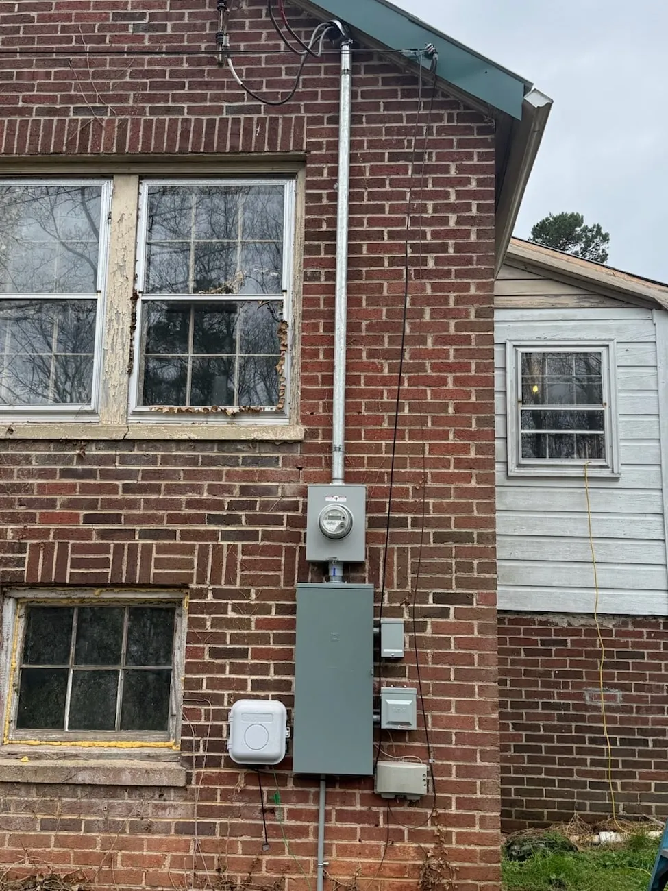A new meter and panel on a brick wall, with the riser pipe running from the meter up to where the service wires attach at the roofline