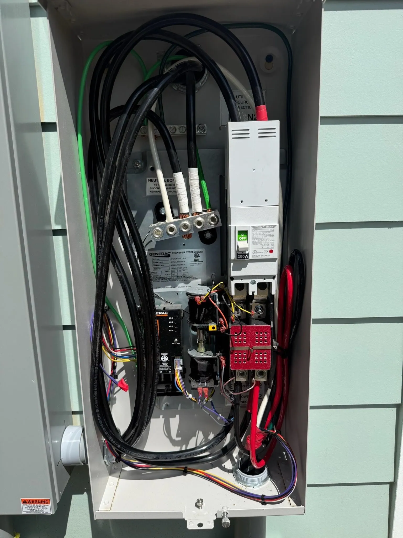 The inside of a transfer switch on the side of a house, with its cables and breakers connected